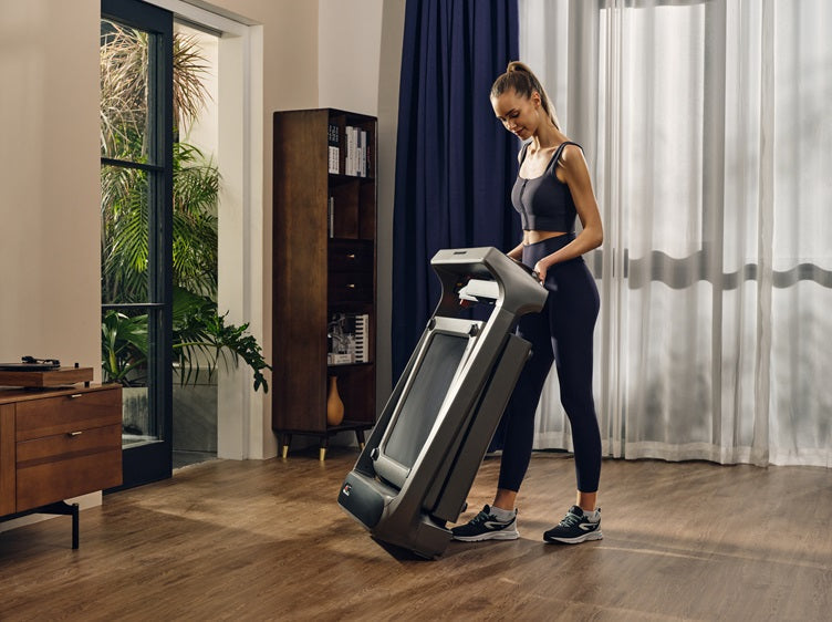 Woman moving the folded WalkingPad X218 tri-fold treadmill for vertical storage at home